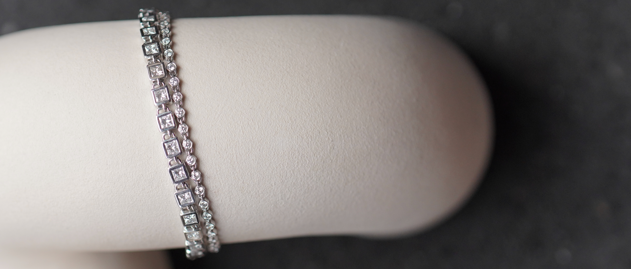Pair of 18k white gold diamond tennis bracelets displayed on white vase.
