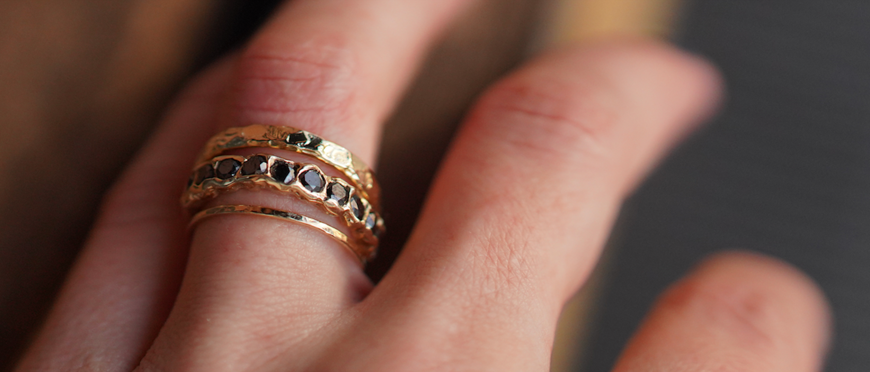 Close-up of a hand wearing a gold ring with black stones.