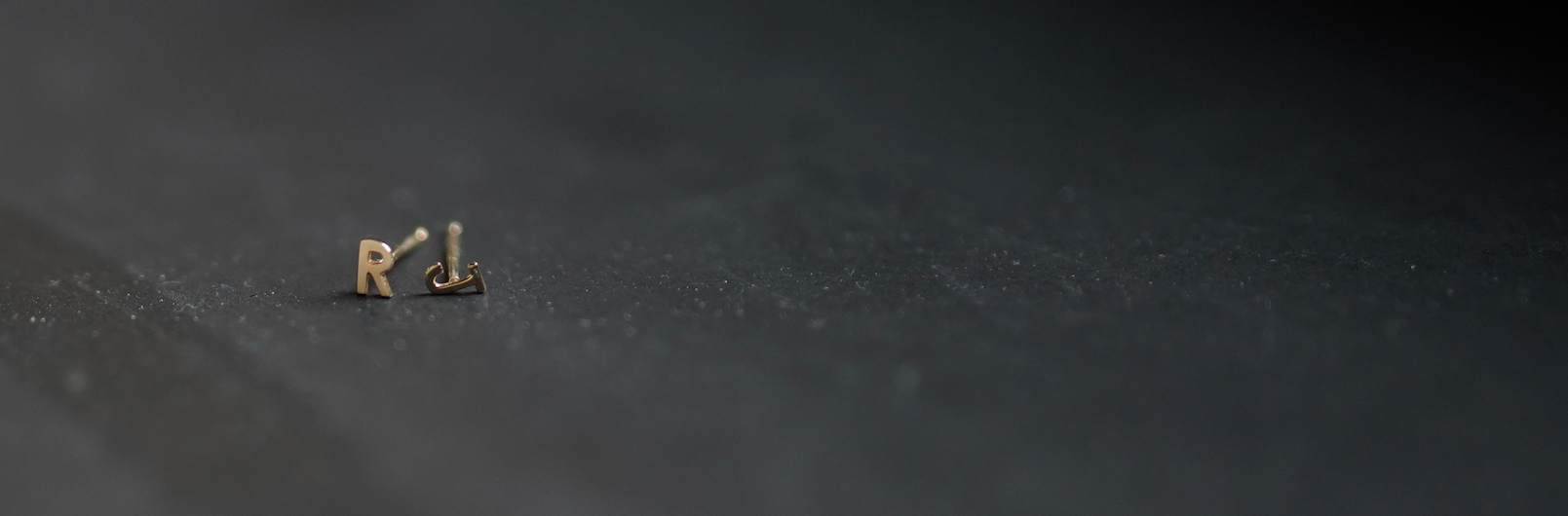 Small gold letter earrings of 'R' and 'L' on a dark background