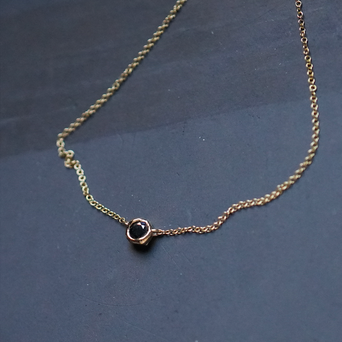 Gold chain necklace with a black gemstone on a dark blue background