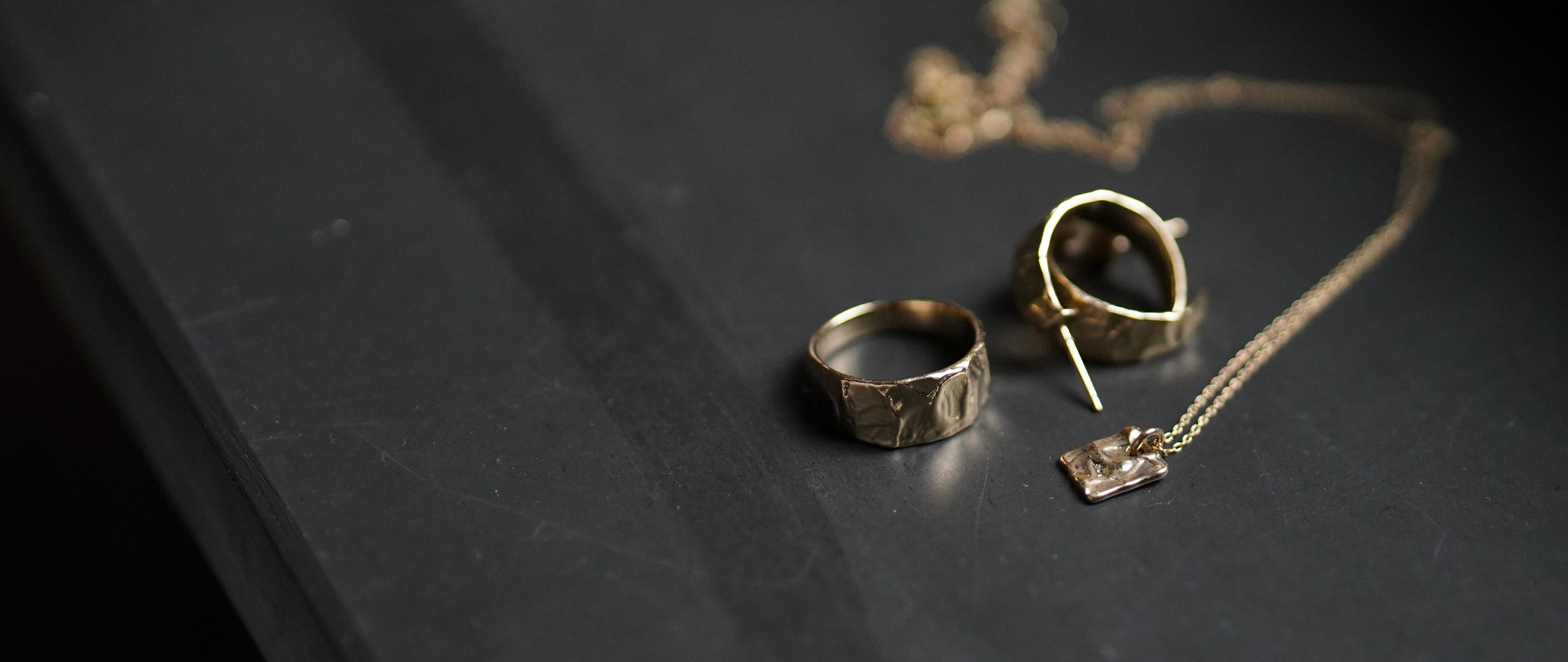 Gold hoop earrings, ring and necklace on a dark surface